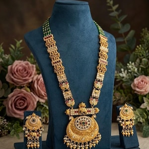 May include: A gold-toned necklace featuring four strands of green beads, ornate rectangular metal segments, and a large crescent-shaped pendant with an elephant motif, accompanied by two matching circular earrings with dangling beads.
