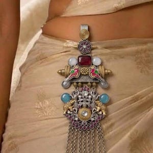 May include: A decorative waist ornament featuring a silver-toned metal base with intricate filigree, inlaid with red, blue, and white stones. The piece includes two bird motifs, two elephant figures, and a series of dangling silver chains with beads.