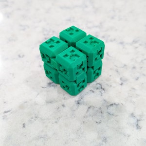 May include: A green 3D printed cube puzzle made of smaller cubes that can be rotated and rearranged.