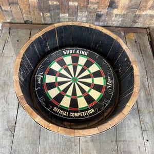 May include: A circular dartboard labeled Shot King and Viper Official Competition with black, white, red, and green segments, mounted inside a dark, charred wooden barrel frame with a natural wood rim, viewed from a high angle.