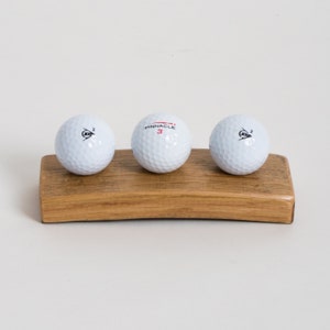 May include: Three white golf balls with black markings on a wooden stand. The middle ball has the word "Pinnacle" and the number "3" printed on it.