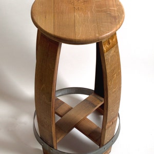 Puede incluir: Un taburete de madera hecho de un barril de vino reutilizado. El taburete tiene un asiento redondo y una banda de metal alrededor de la parte inferior.