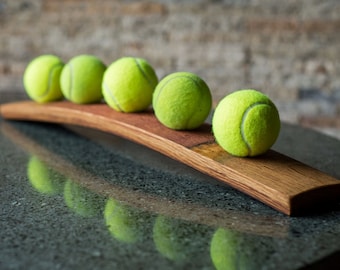 May include: Five yellow tennis balls are arranged on a curved wooden stand. The stand is made from a piece of reclaimed wood.