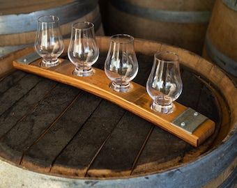 May include: A wooden whiskey tasting tray with four small glasses, resting on top of a wooden barrel.