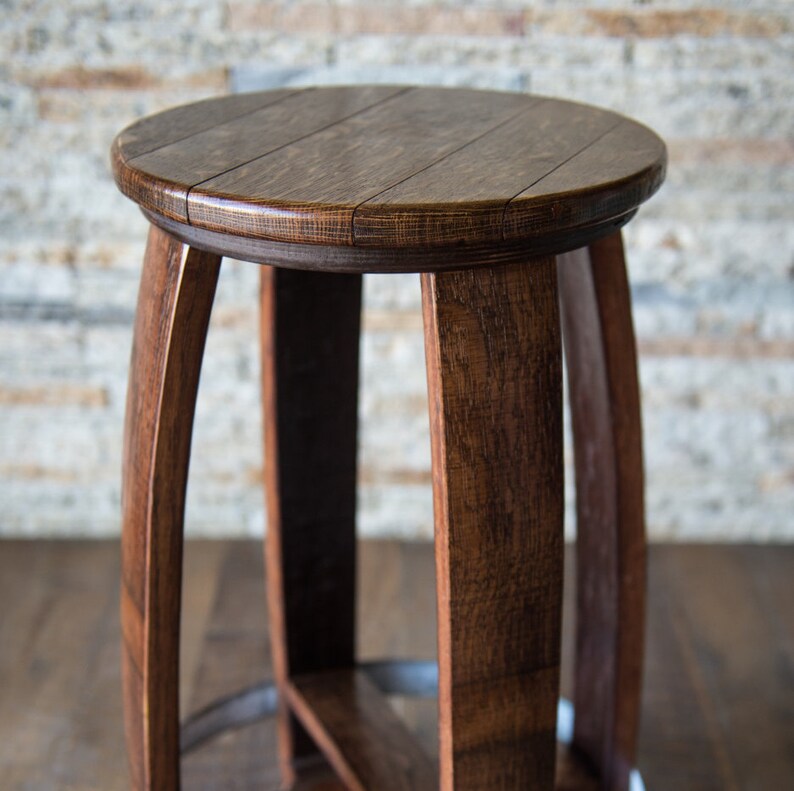 Puede incluir: Un taburete de madera marr&oacute;n oscuro con una parte superior redonda y un dise&ntilde;o simple. El taburete est&aacute; hecho de madera reciclada y tiene un aspecto r&uacute;stico.