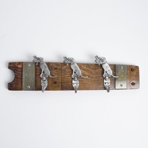 May include: A wooden coat rack with three hooks shaped like dogs. The hooks are made of metal and have a silver finish. The rack is made of reclaimed wood and has a rustic look.