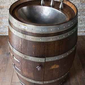 May include: A wooden barrel sink with a hammered copper basin and three silver faucets. The barrel has metal bands and a small grape-shaped knob on the door.
