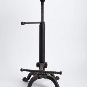 May include: A black metal adjustable bar stool with a wooden seat. The stool has a hand crank to adjust the height. The base of the stool has a unique, twisted design.