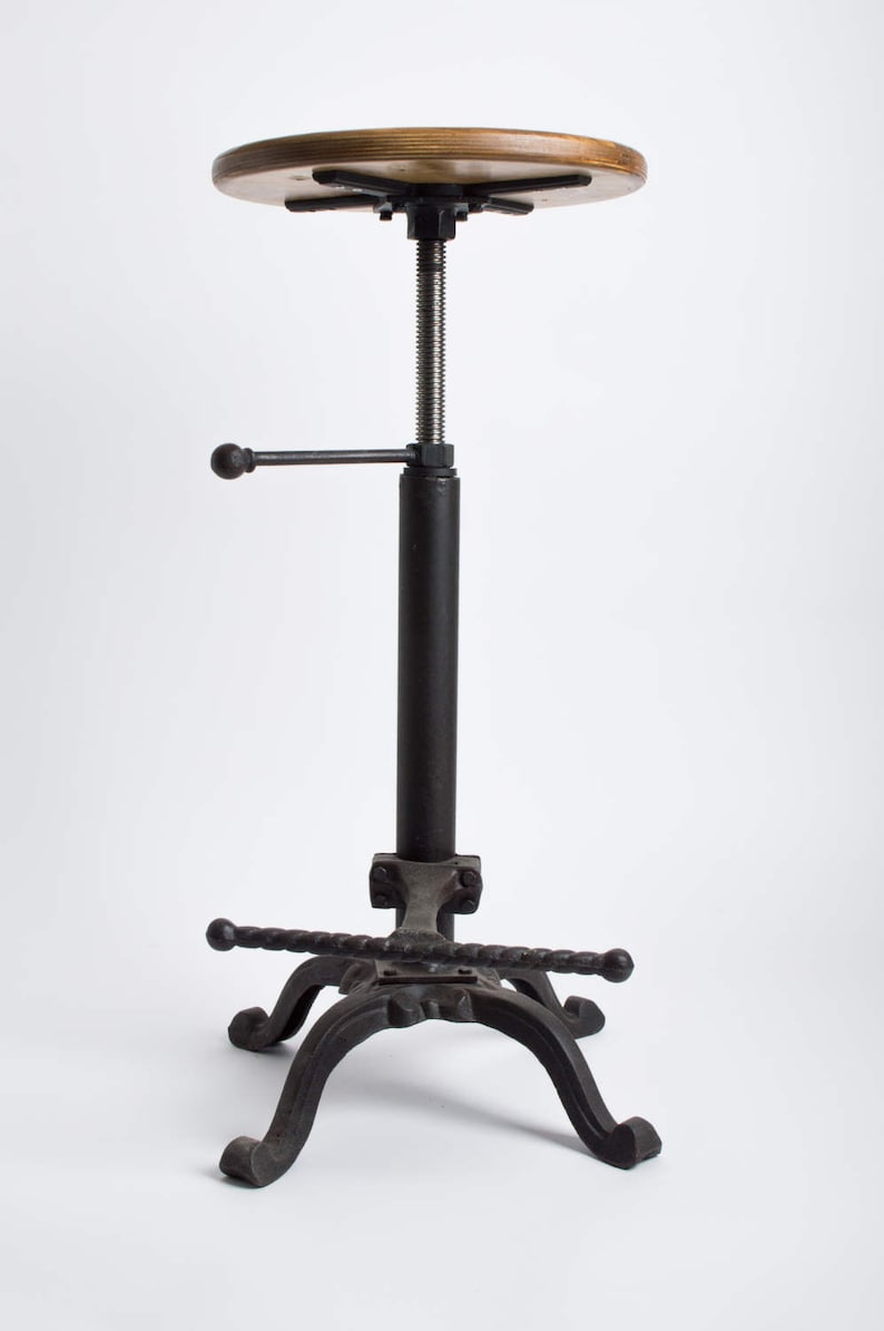 May include: A black metal adjustable bar stool with a wooden seat. The stool has a hand crank to adjust the height. The base of the stool has a unique, twisted design.