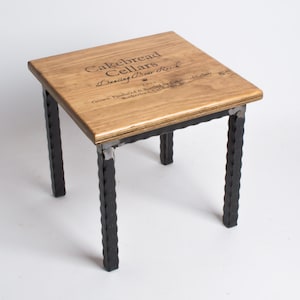 May include: A small wooden table with black metal legs. The tabletop is made from a repurposed wine crate with the text "Cakebread Cellars Dancing Pear Ranch 2010 Grown, Produced & Bottled by Cakebread Cellars Rutherford, California" printed on it.