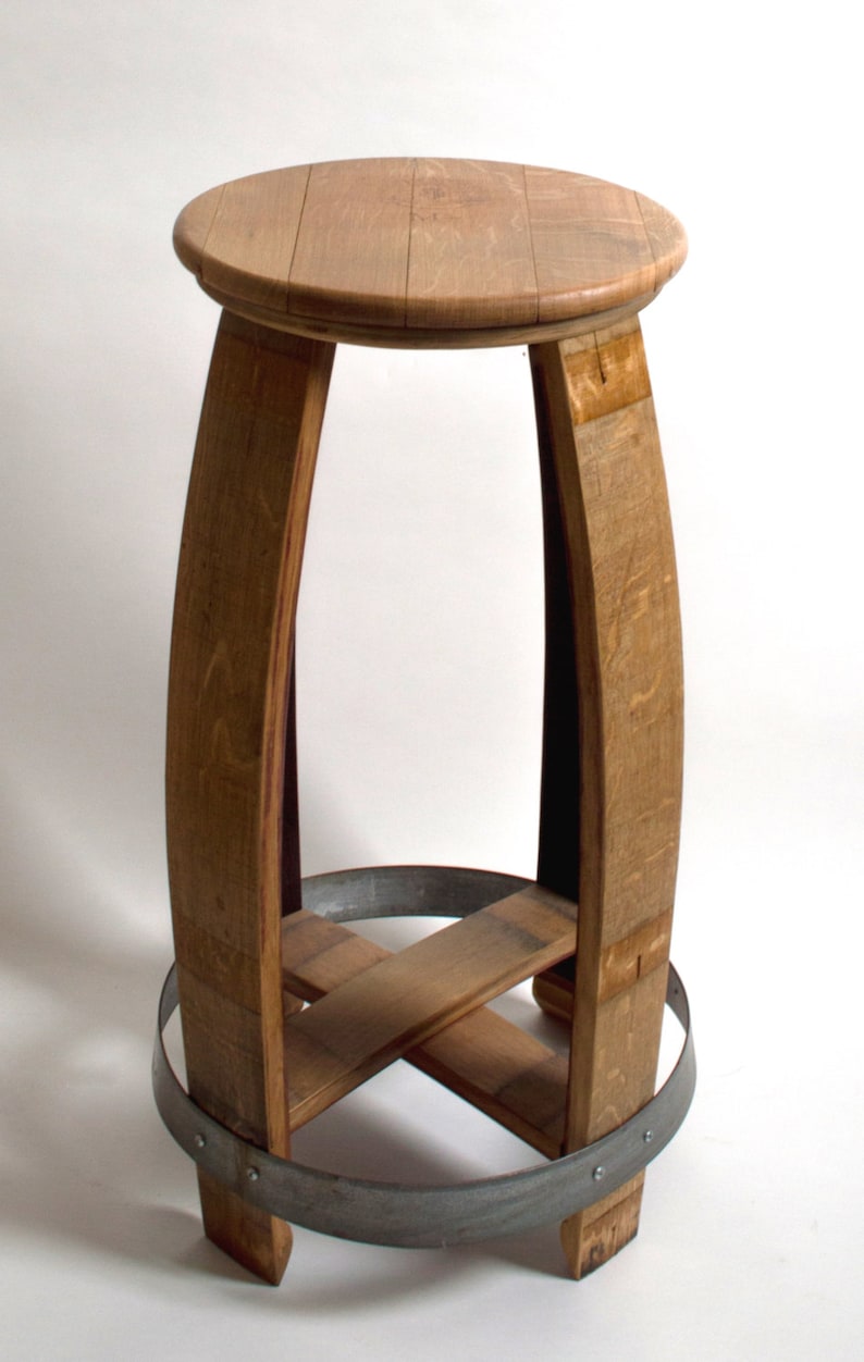 Puede incluir: Un taburete de madera hecho de un barril de vino reutilizado. El taburete tiene un asiento redondo y una base de metal.