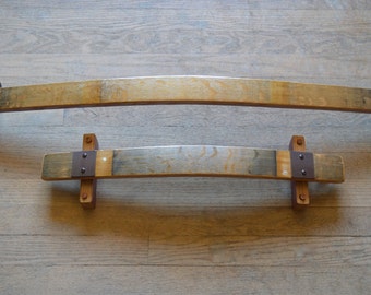 May include: Two wooden shelf brackets made from reclaimed wine barrels. The larger bracket is curved and the smaller bracket is straight. Both brackets have metal accents.
