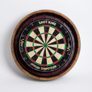 May include: A round dartboard with a black and tan target, surrounded by a wooden barrel frame. The dartboard has red and green rings, with the text "SHOP KING" and "OFFICIAL COMPETITION". The brand "Viper" is also visible.