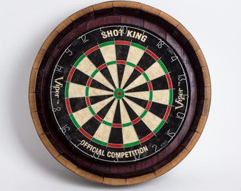 Puede incluir: Un tablero de dardos redondo con un objetivo negro y beige, rodeado por un marco de barril de madera. El tablero de dardos tiene anillos rojos y verdes, con el texto "SHOP KING" y "OFFICIAL COMPETITION". La marca "Viper" también es visible.