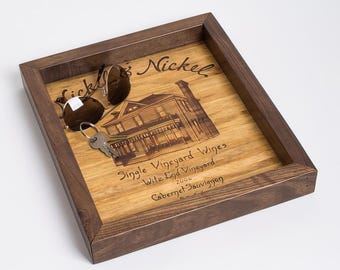 May include: A square wooden tray with a dark brown frame and a light wood base. The base features a printed illustration of a house and text reading Nickel & Nickel, Single Vineyard Wines, Witz End Vineyard, 2006, Cabernet Sauvignon. Sunglasses and keys rest inside.