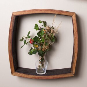 May include: A rustic wooden wall shelf made from a reclaimed wine barrel with a curved top and a small glass vase with dried flowers and berries.