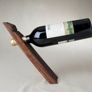 May include: A wooden wine bottle holder with a dark brown finish. The holder is shaped like a slanted 'V' and is designed to hold a bottle of wine horizontally.