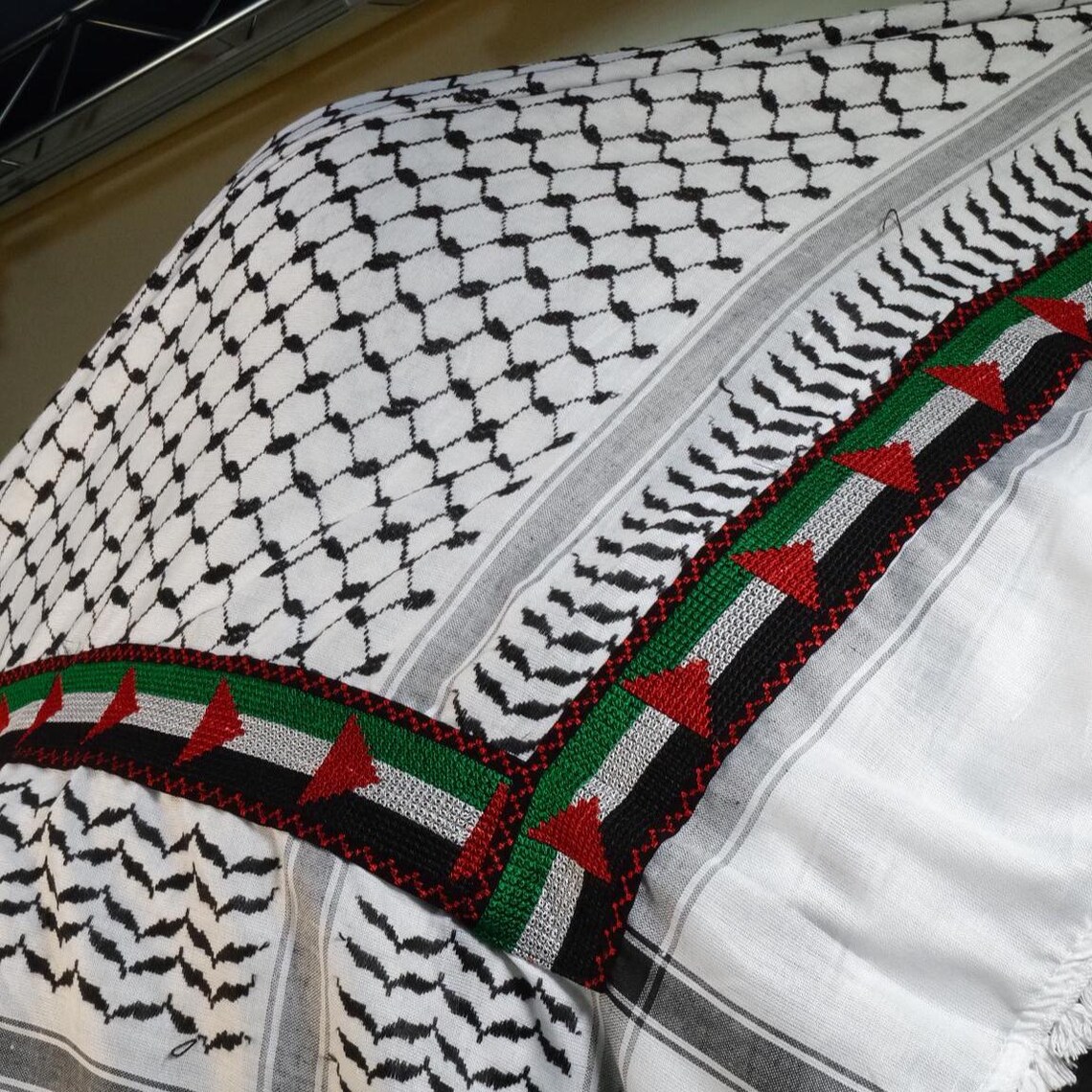 كوفية فلسطينية بيضاء وسوداء مطوية بنقشة هندسية تقليدية وتفاصيل شرّابات (3)