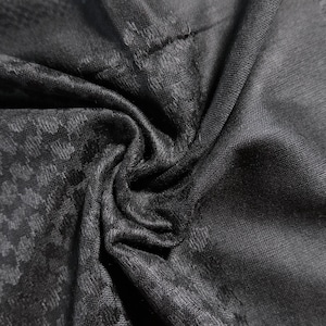 Könnte beinhalten: Nahaufnahme eines dunkelgrauen Stoffes mit strukturiertem Muster. Der Stoff ist drapiert und zeigt Falten und Variationen von Licht und Schatten. Das Muster scheint ein kleines, sich wiederholendes geometrisches Design zu sein.