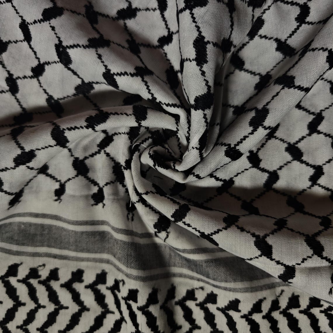 كوفية فلسطينية بيضاء وسوداء مطوية بنقشة هندسية تقليدية وتفاصيل شرّابات (2)