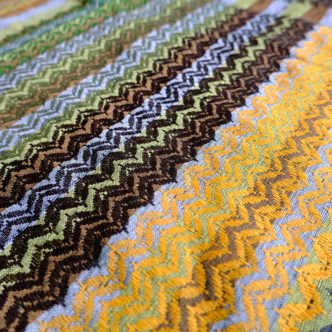 لقطة قريبة لكوفية ملوّنة بنقوش متعرجة ومربعات بدرجات البني والأخضر والأصفر والبرتقالي (4)