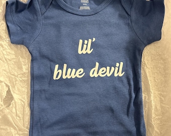 May include: A blue baby onesie with the text "lil' blue devil" in white. The onesie has short sleeves and snaps at the bottom. The fabric appears to be soft and comfortable.