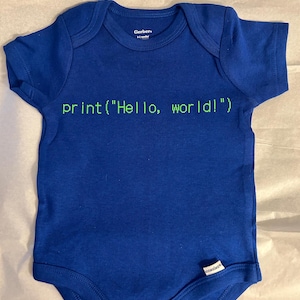 May include: A blue baby onesie with short sleeves. The text "print("Hello, world!")" is printed in green across the front. The onesie has a snap closure at the bottom and the brand name "Gerber" is visible.