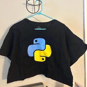 May include: Black crop top with a blue and yellow Python programming language logo. The shirt is hanging on a light blue hanger.