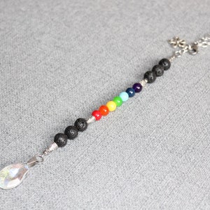 May include: A chakra crystal suncatcher with a silver chain and a teardrop-shaped crystal pendant. The suncatcher features black lava beads and a row of colorful beads in the colors of the rainbow.