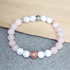May include: A beaded bracelet featuring pink and white stone beads. The bracelet has a mix of smooth, round pink beads and white, marbled beads. A few rose gold and silver beads are interspersed throughout the design. The bracelet is displayed on a neutral background.