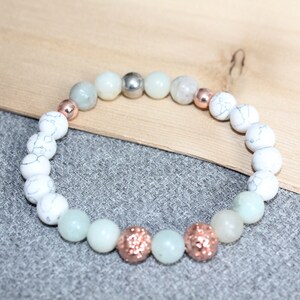 May include: A beaded bracelet featuring a mix of white, light green, and rose gold beads. The bracelet includes white marble-like beads, light green beads, and rose gold glitter beads. A silver bead is also included.