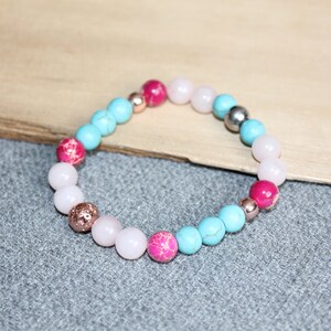 May include: A beaded bracelet featuring a mix of turquoise, pink, and light pink beads. The bracelet includes metallic beads in silver and rose gold. The beads are strung together to form a circular shape, suitable for wrist wear.