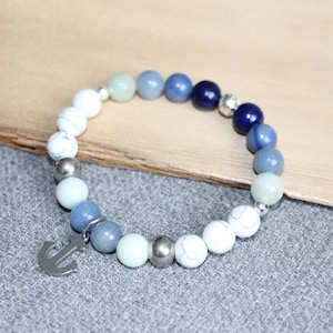 May include: A beaded bracelet featuring a nautical theme. The bracelet has a mix of white, blue, and silver beads, with a silver anchor charm. The beads are various sizes and shades of blue, creating a gradient effect.