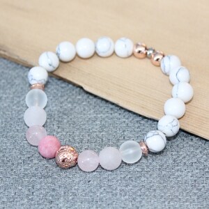 May include: A beaded bracelet featuring white and rose quartz beads, accented with rose gold-colored metal spacers. The bracelet includes a mix of opaque and translucent beads, creating a delicate and stylish accessory.