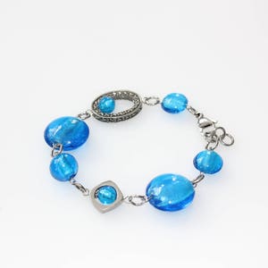 Pu&ograve; includere: Bracciale con perline blu brillante, ovali e rotonde, collegate da una catena color argento. Il bracciale include maglie decorative e una chiusura sicura. Le perline sono di vetro.