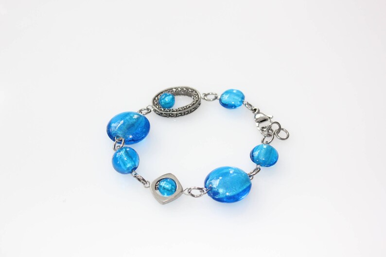 Pu&ograve; includere: Bracciale con perline blu brillante, ovali e rotonde, collegate da una catena color argento. Il bracciale include maglie decorative e una chiusura sicura. Le perline sono di vetro.