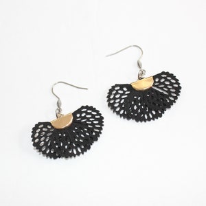 May include: A pair of black, fan-shaped earrings with a perforated design. Each earring has a gold-colored half-circle accent at the top and a silver-colored hook. The earrings are displayed on a white background.