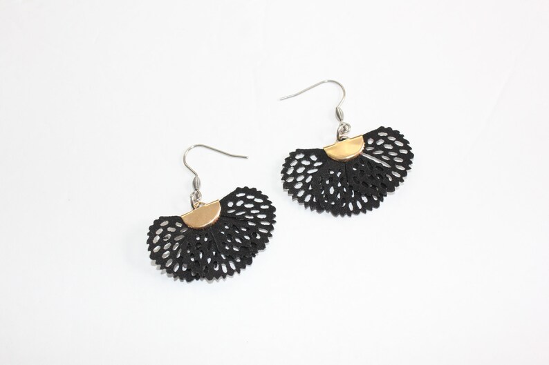 May include: A pair of black, fan-shaped earrings with a perforated design. Each earring has a gold-colored half-circle accent at the top and a silver-colored hook. The earrings are displayed on a white background.