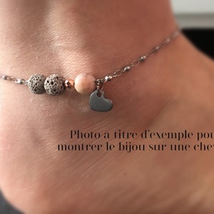 Puede incluir: Pulsera de tobillo con cadena plateada, con cuentas de roca volc&aacute;nica gris, una gema rosa y un peque&ntilde;o dije de coraz&oacute;n. La pulsera se muestra en un tobillo.