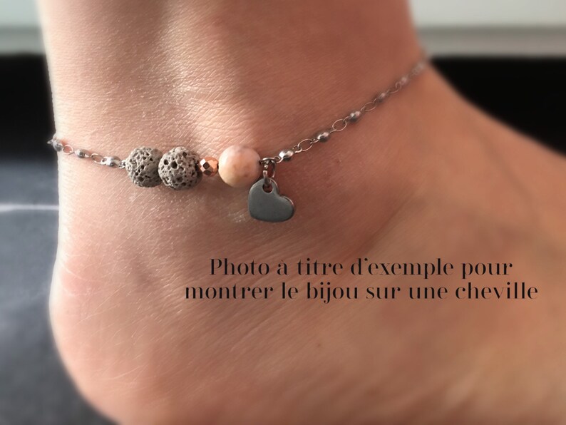 Puede incluir: Pulsera de tobillo con cadena plateada, con cuentas de roca volc&aacute;nica gris, una gema rosa y un peque&ntilde;o dije de coraz&oacute;n. La pulsera se muestra en un tobillo.