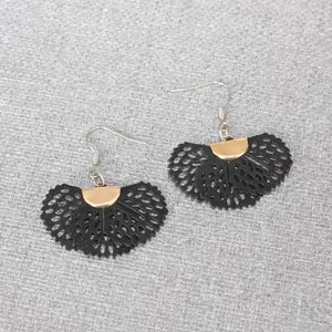 May include: A pair of black, fan-shaped earrings with a gold-colored accent at the top. The earrings have a delicate, openwork design and silver-colored ear wires. The earrings are displayed on a gray textured surface.