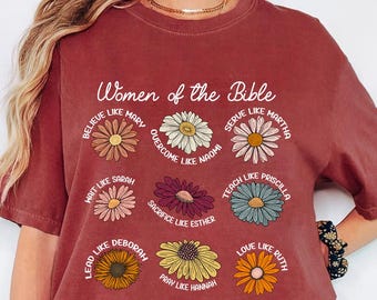 May include: Brick-colored t-shirt featuring the text "Women of the Bible" above nine daisy illustrations. Each daisy has a different name and phrase, such as "Believe like Mary" and "Serve like Martha".