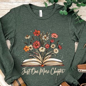 May include: A long-sleeved, heather forest green t-shirt with a floral design and an open book. The text "Just One More Chapter" is printed below the book.
