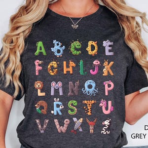 K&ouml;nnte beinhalten: Dunkelgraues Heather-T-Shirt mit einem farbenfrohen Tieralphabet-Design. Jeder Buchstabe ist als ein anderes Tier dargestellt. Der Text "DARK GREY HEATHER" ist unten rechts aufgedruckt. Ein lustiges und lehrreiches Kleidungsst&uuml;ck.