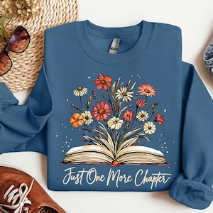 May include: Indigo blue sweatshirt with a floral design and an open book with the text "Just One More Chapter".