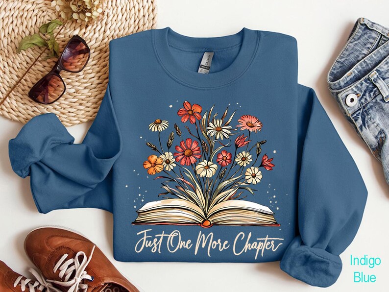 May include: Indigo blue sweatshirt with a floral design and an open book with the text "Just One More Chapter".
