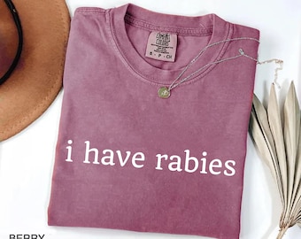 Peut inclure: Un t-shirt à manches courtes de couleur baie avec un col rond et le texte blanc "i have rabies" imprimé sur la poitrine. Le t-shirt présente une étiquette de marque Comfort Colors à l'intérieur du col indiquant une taille S, 100% coton.