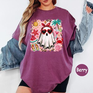 Peut inclure: Un t-shirt couleur baie avec une impression graphique repr&eacute;sentant un fant&ocirc;me portant un bandana rouge et des lunettes de soleil en forme de c&oelig;ur. Le motif inclut des &eacute;l&eacute;ments estivaux comme un palmier, une &eacute;toile de mer et un cocktail.