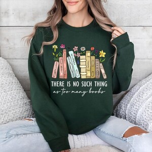 May include: Forest green sweatshirt with the text "THERE IS NO SUCH THING as too many books" in white script. The design features a row of illustrated books with flowers.