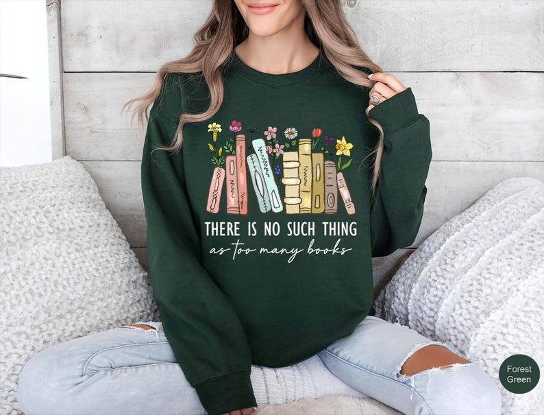 May include: Forest green sweatshirt with the text "THERE IS NO SUCH THING as too many books" in white script. The design features a row of illustrated books with flowers.